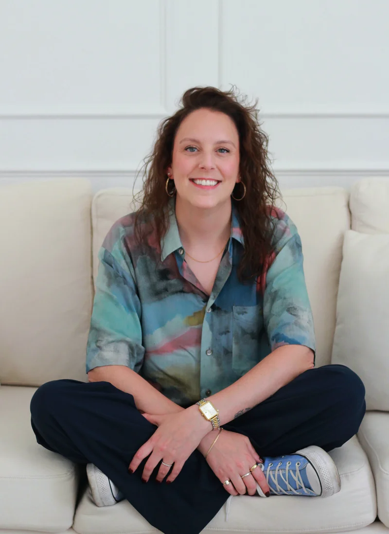 Breana Rutledge, Registered Psychotherapist, seated cross-legged on a couch, smiling
