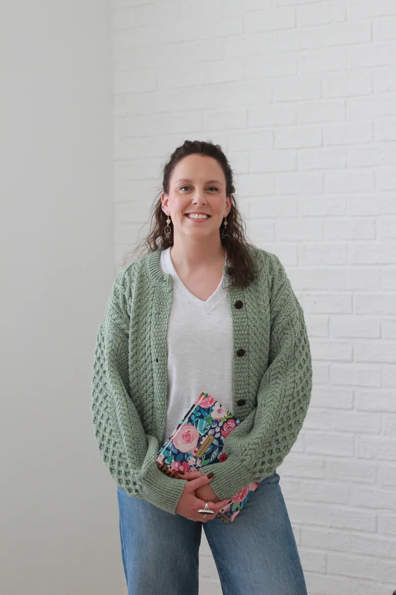 Breana Rutledge, Registered Psychotherapist, holding a notebook in a soft green sweater